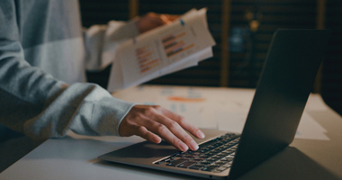 Using laptop and looking at paperwork with graphs