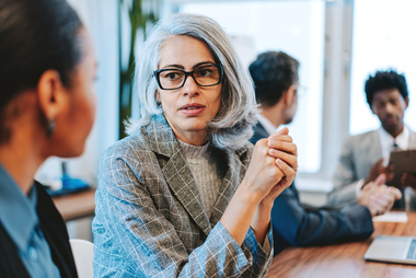 Older business professional seated talking to younger business professional